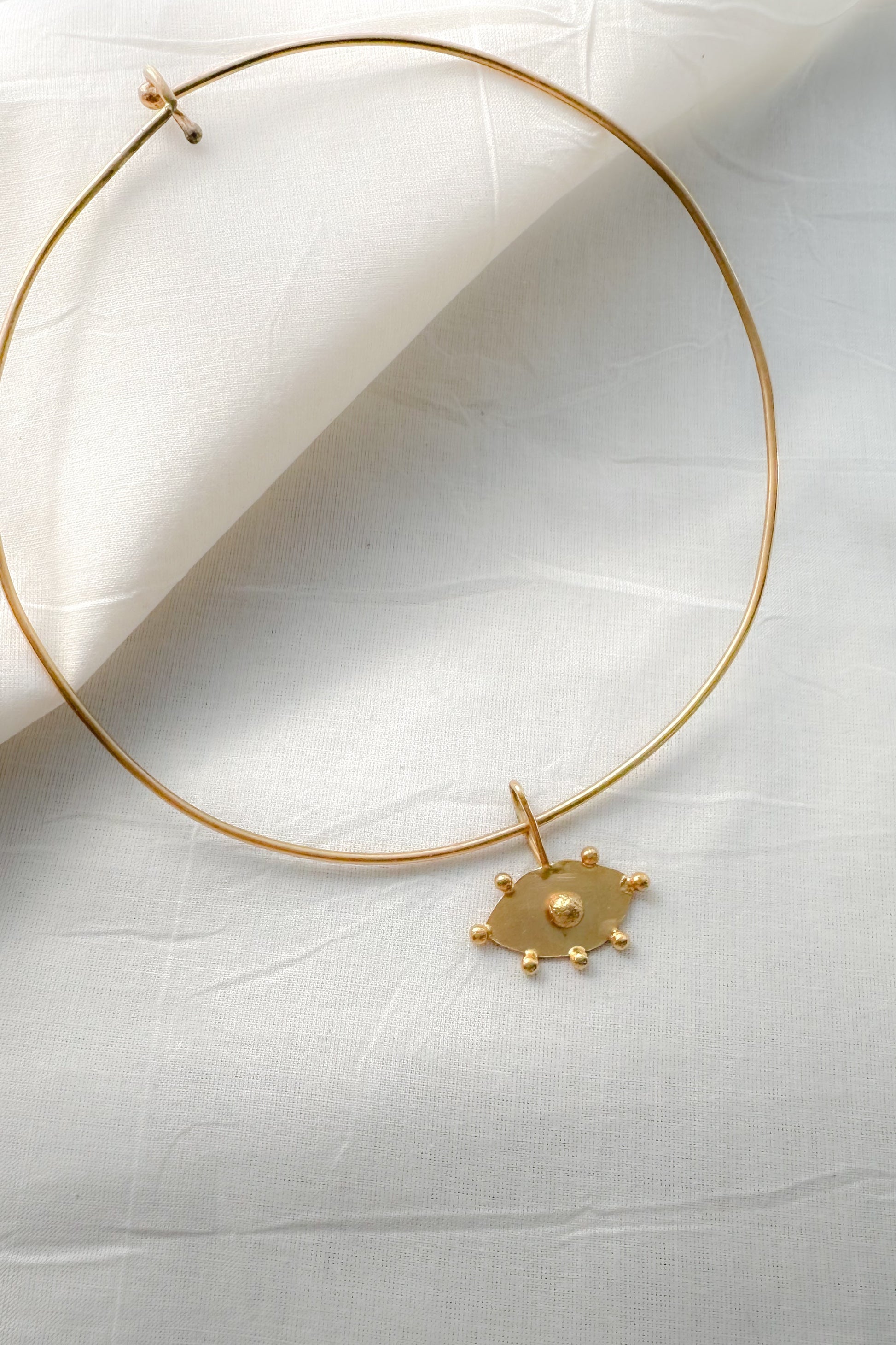 Gold choker necklace with evil eye pendant on a white fabric background