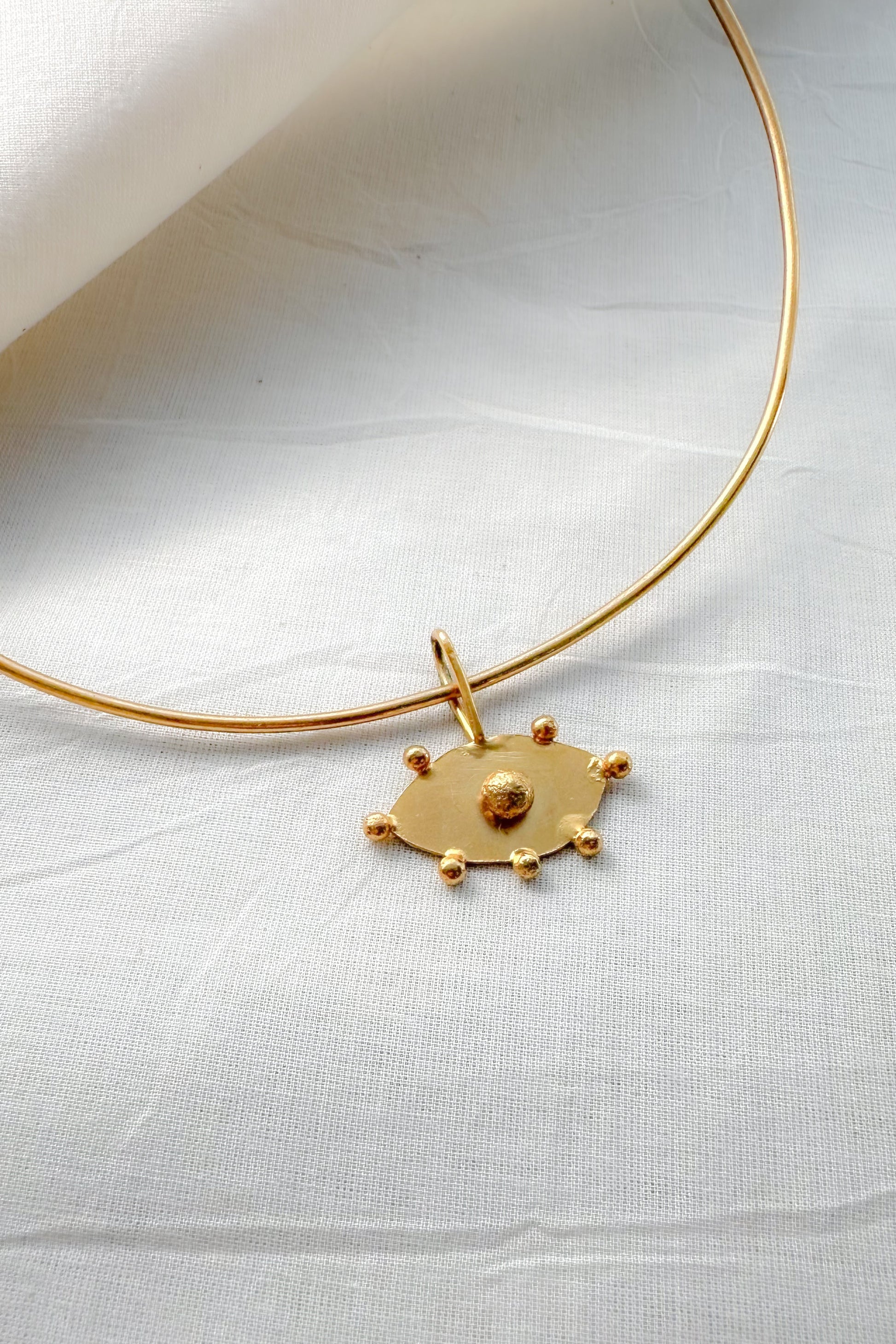 Gold choker necklace with evil eye pendant on a white fabric background