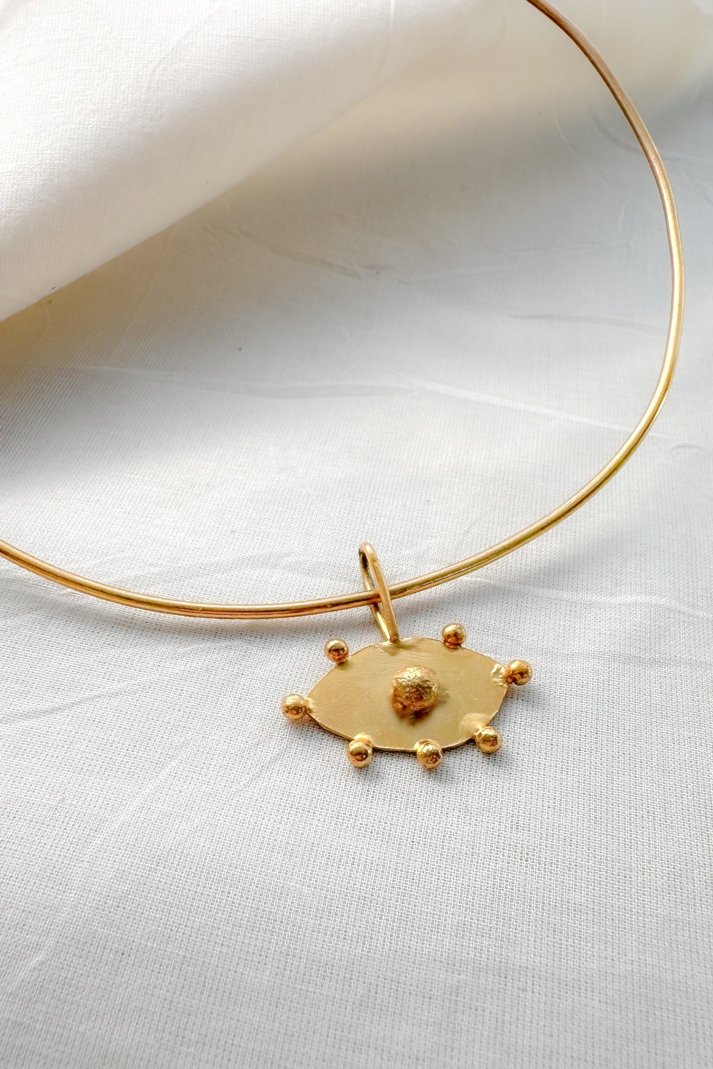 Gold choker necklace with evil eye pendant on a white fabric background