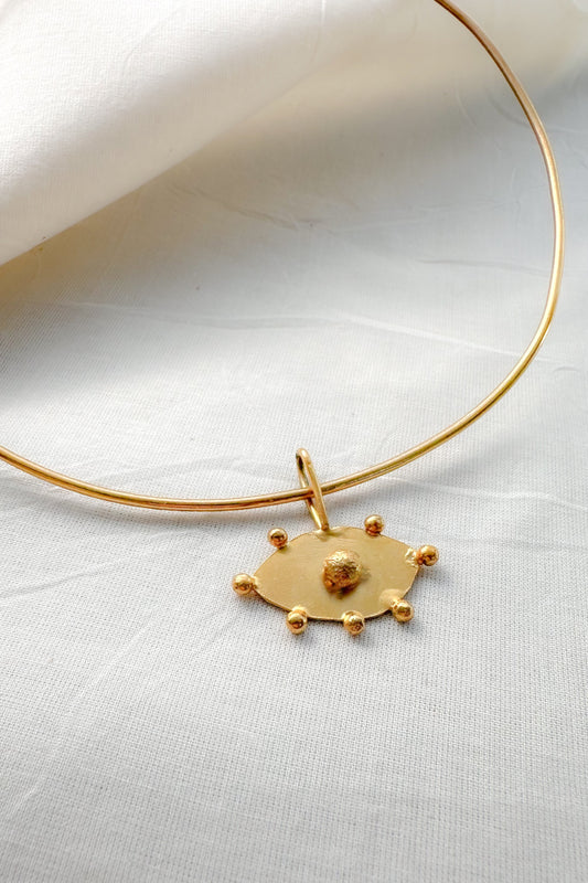 Gold choker necklace with evil eye pendant on a white fabric background
