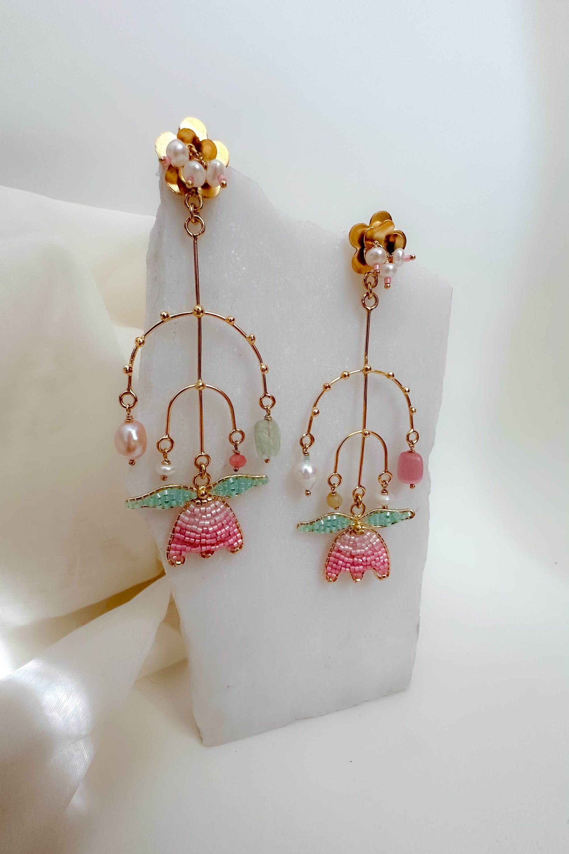 Gold earrings with pink and green accents on a white stand