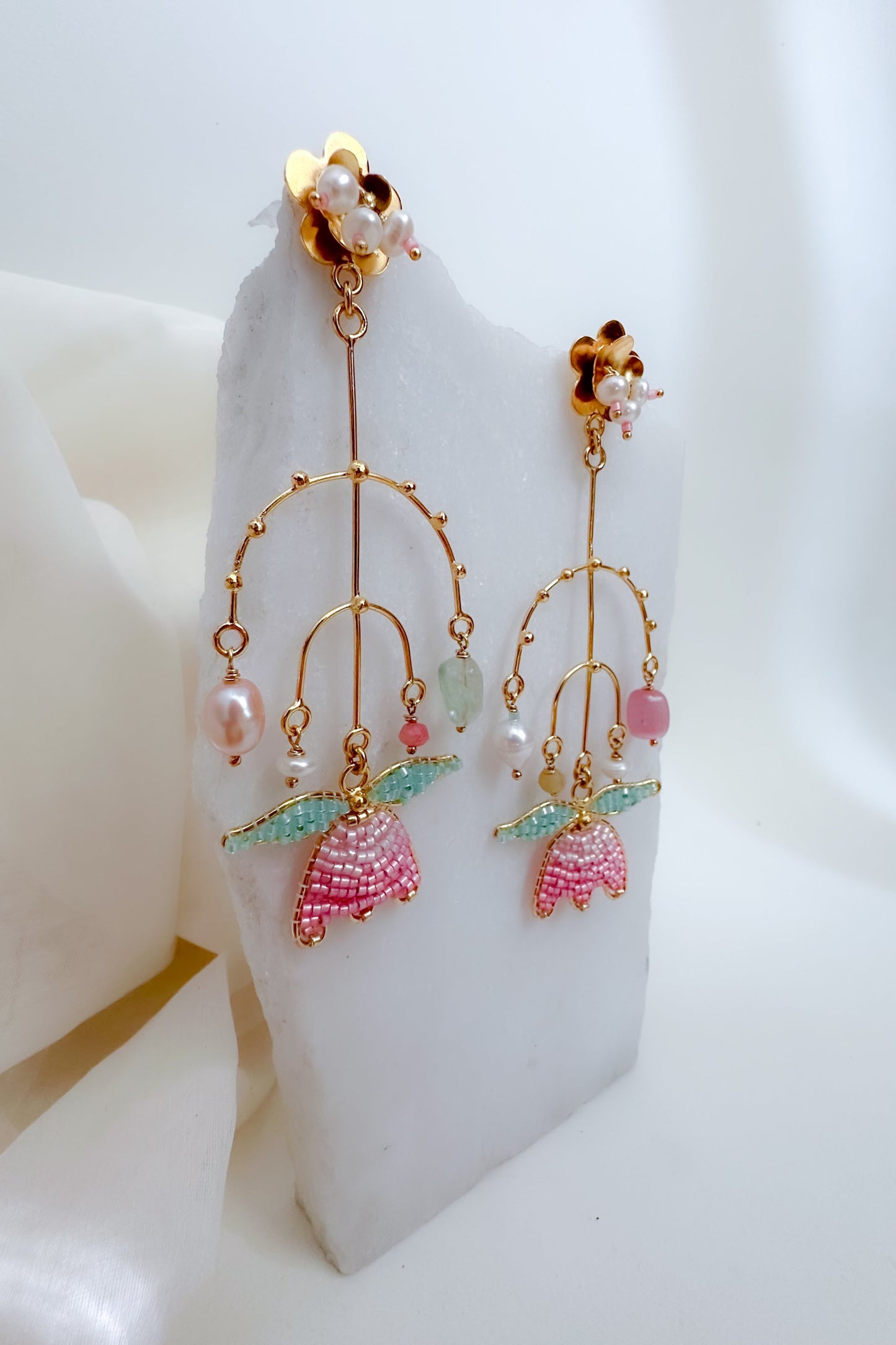 Pair of earrings with pink and green accents on a white stand