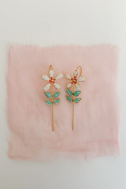 Pair of floral earrings with green and red accents on a pink fabric background