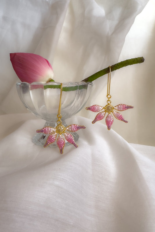 Pink lotus earrings on a white surface with a pink flower petal.
