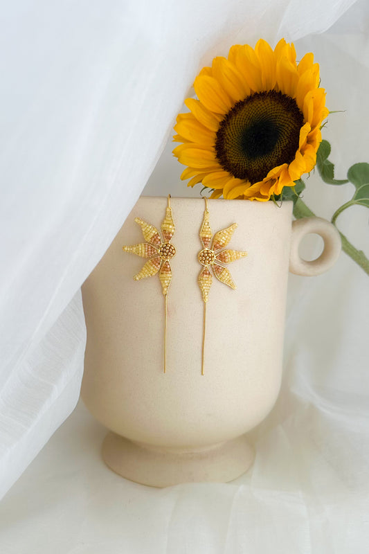 Gold earrings on a white vase with a sunflower against a white background