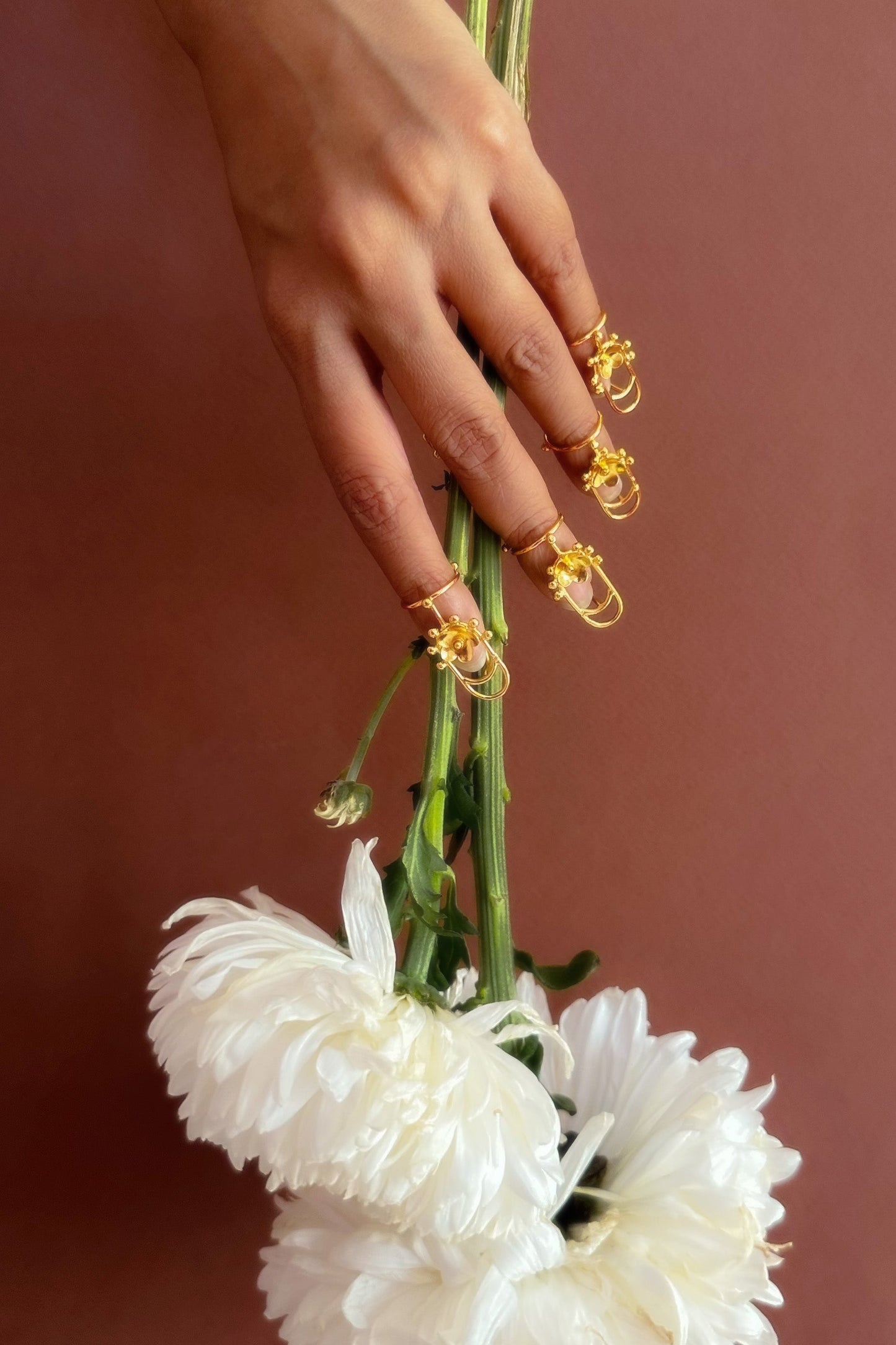 Hand holding a bouquet of white flowers with gold accents against a brown background