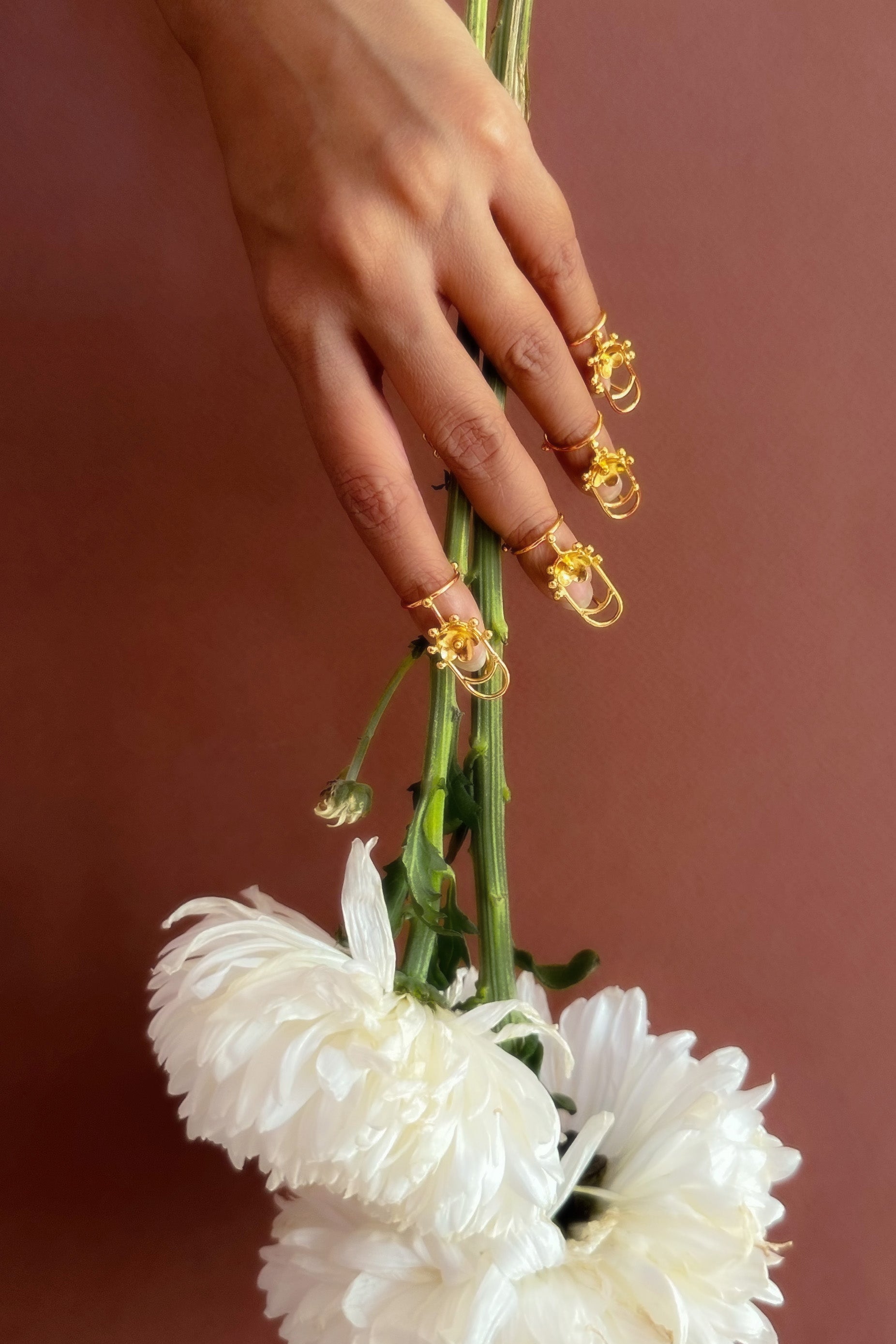Hand holding a bouquet of white flowers with gold accents against a brown background