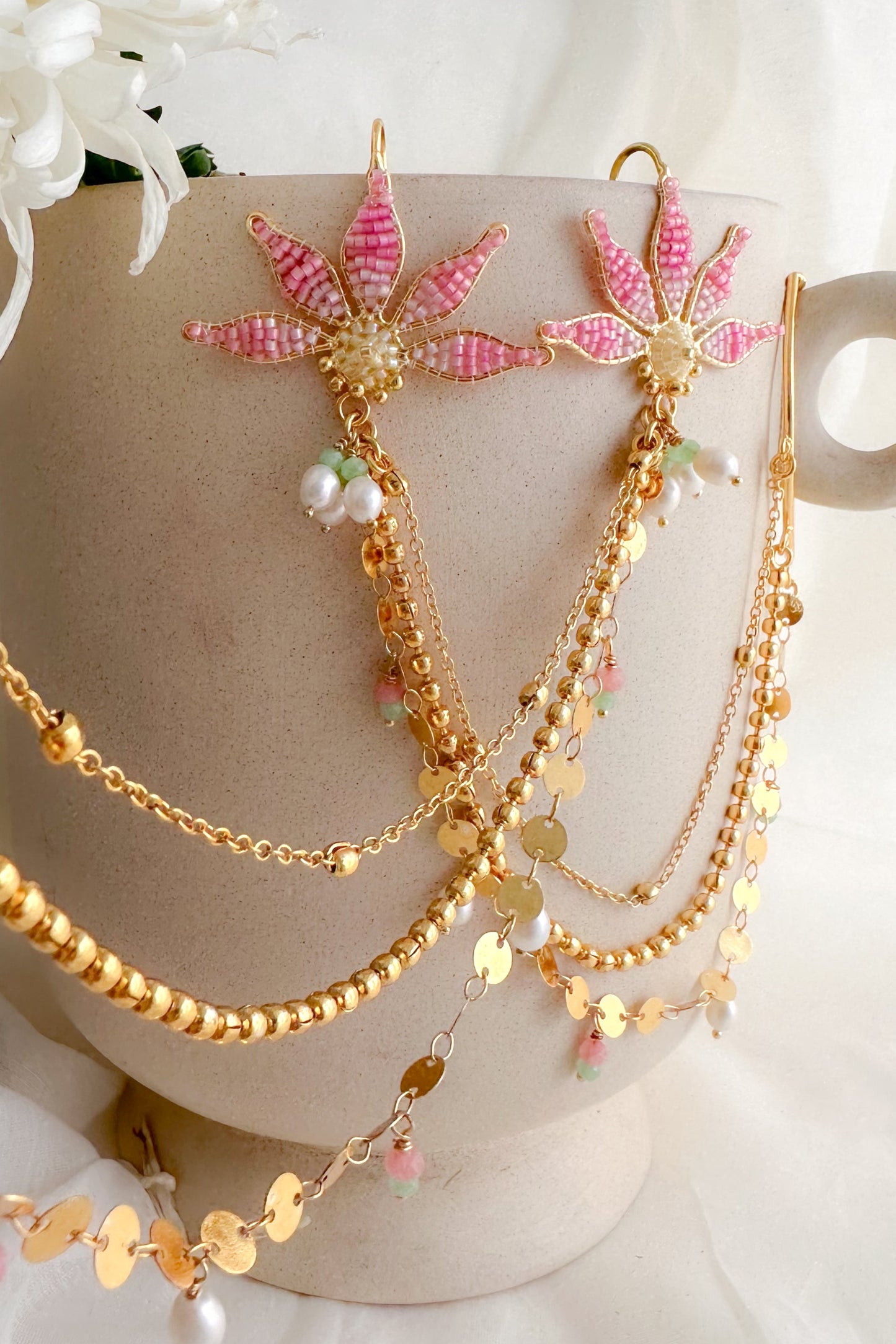 Gold and pink floral jewelry set on a mannequin head with white flowers in the background