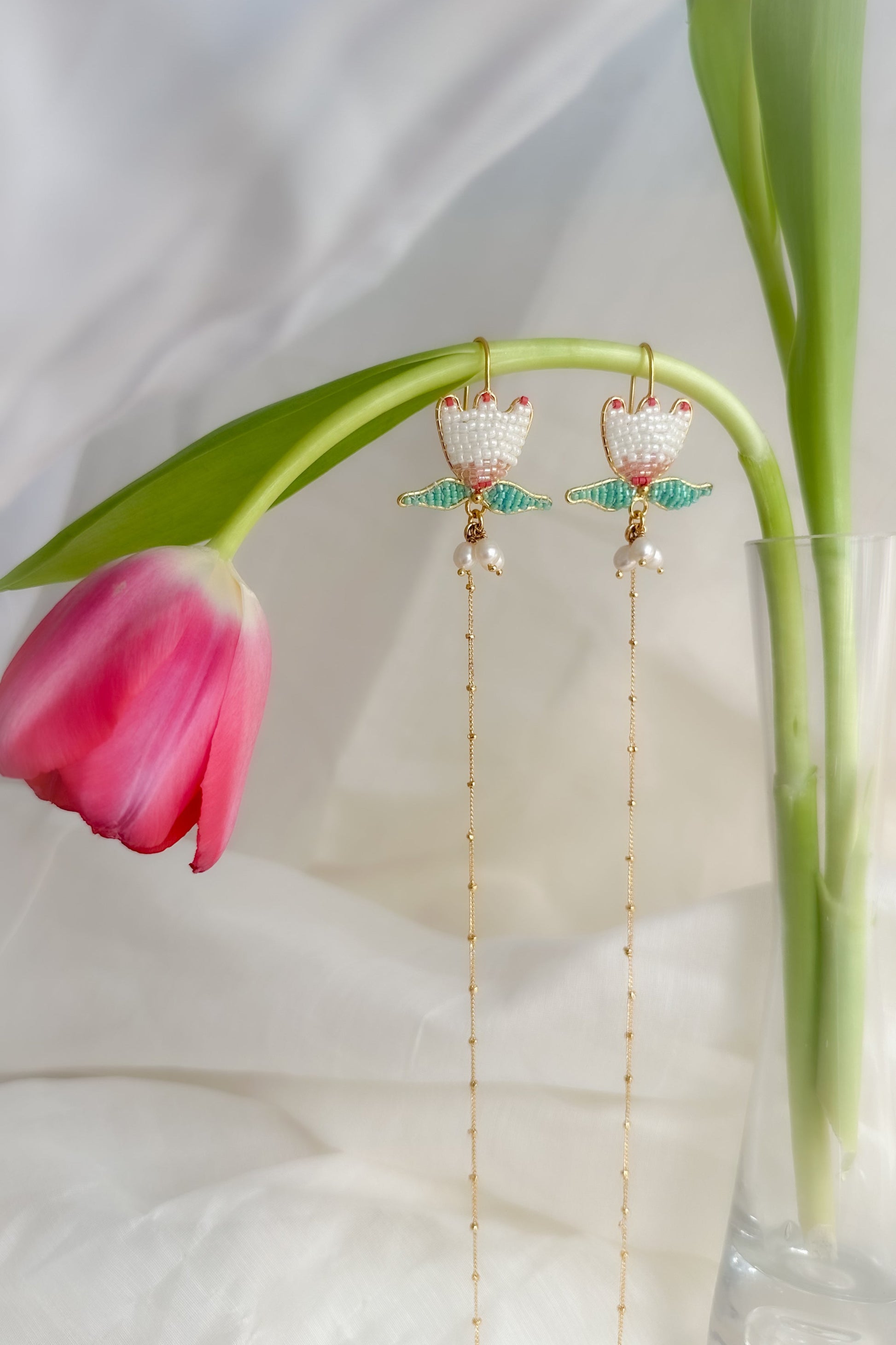 Gold earrings with green accents on a white background with pink tulips