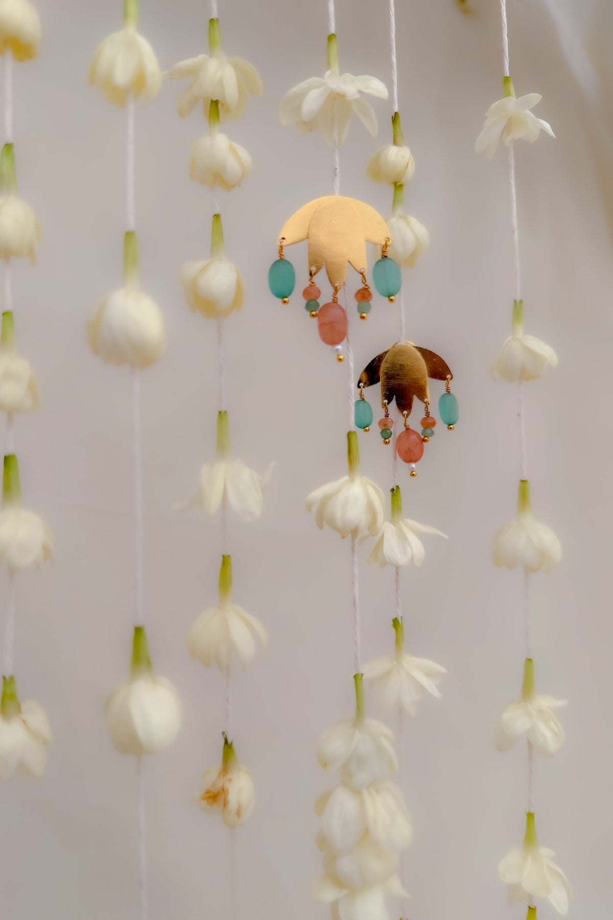 A close-up of a decorative hanging ornament featuring multiple strands of white flower buds suspended vertically, with a central yellow crescent moon and bird charm decorated with turquoise and peach beads.