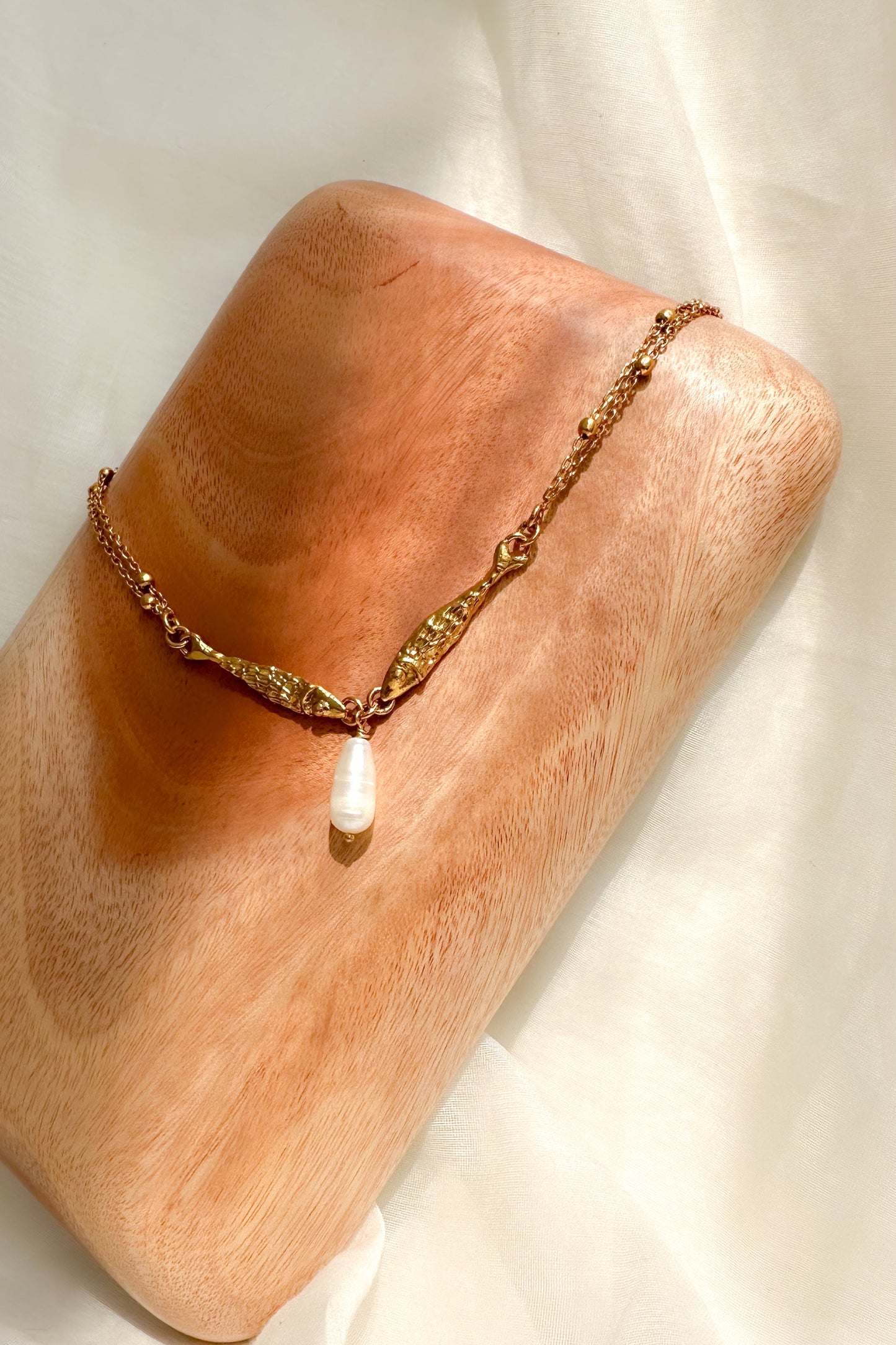 Gold necklace on a wooden block with a white fabric background