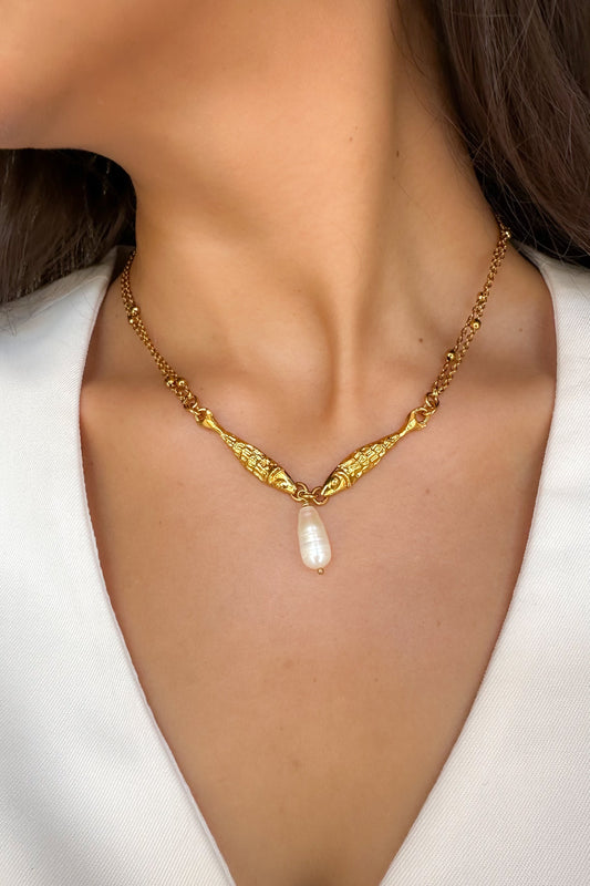 Gold necklace with a pearl pendant on a person wearing a white top.