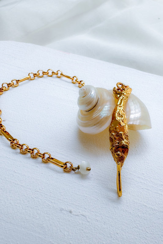 A gold chain bracelet featuring fish charm, displayed on a soft white fabric background.