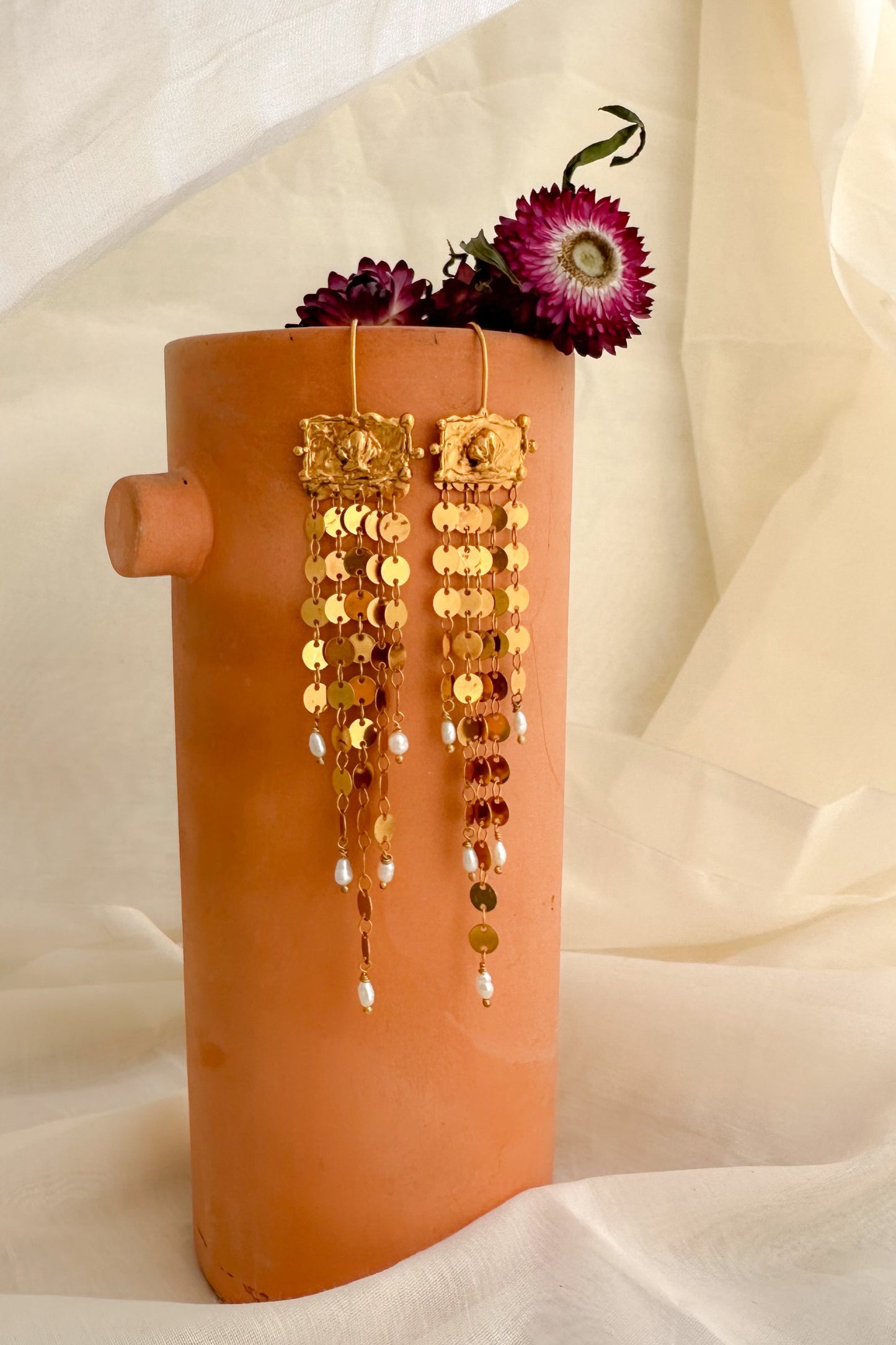 Terracotta vase with gold earrings and purple flowers on a white background