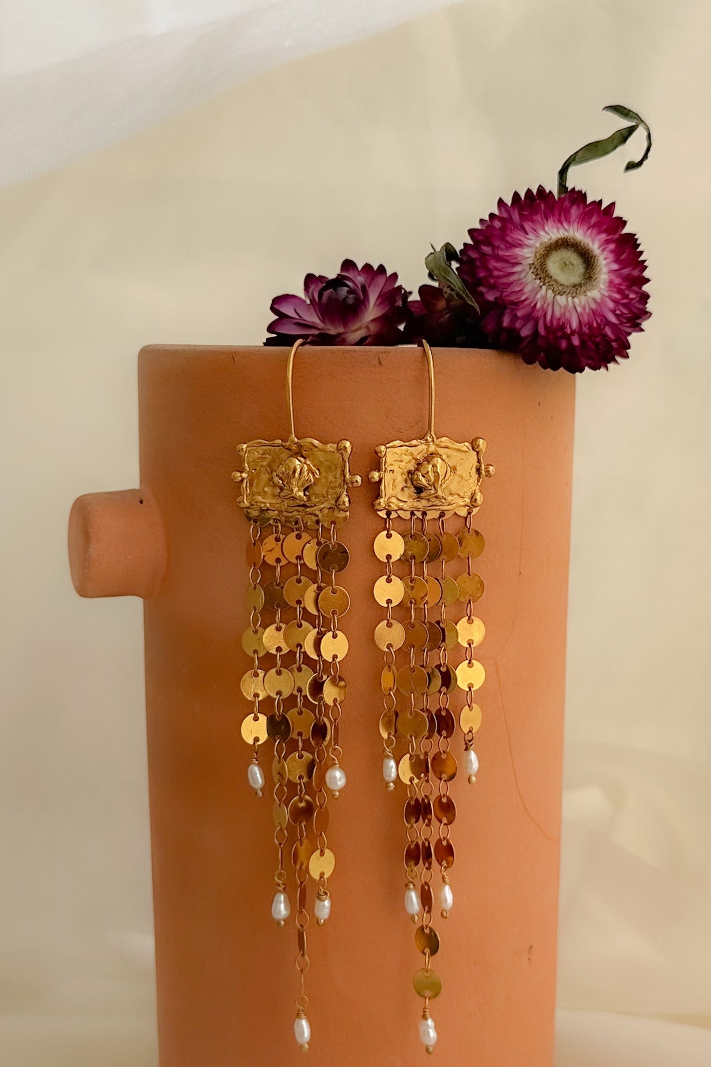 Gold earrings on a pink stand with flowers against a beige fabric background